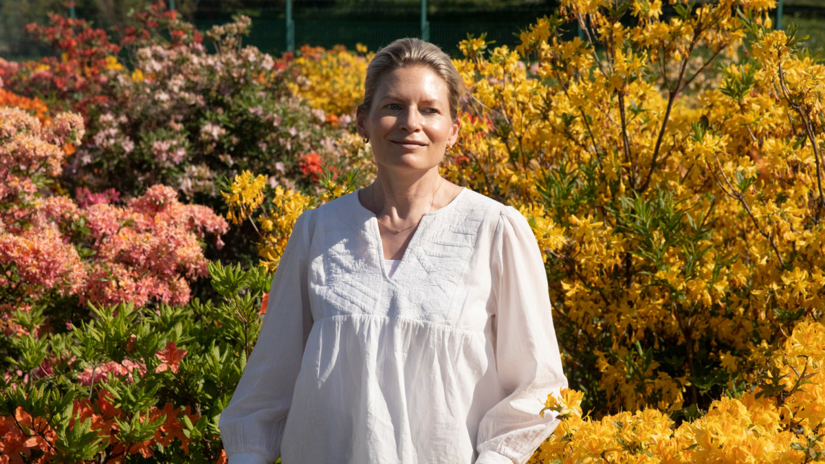 Anna-Liisa Laine looks at the camera in front of vibrant flowers in Viikki.